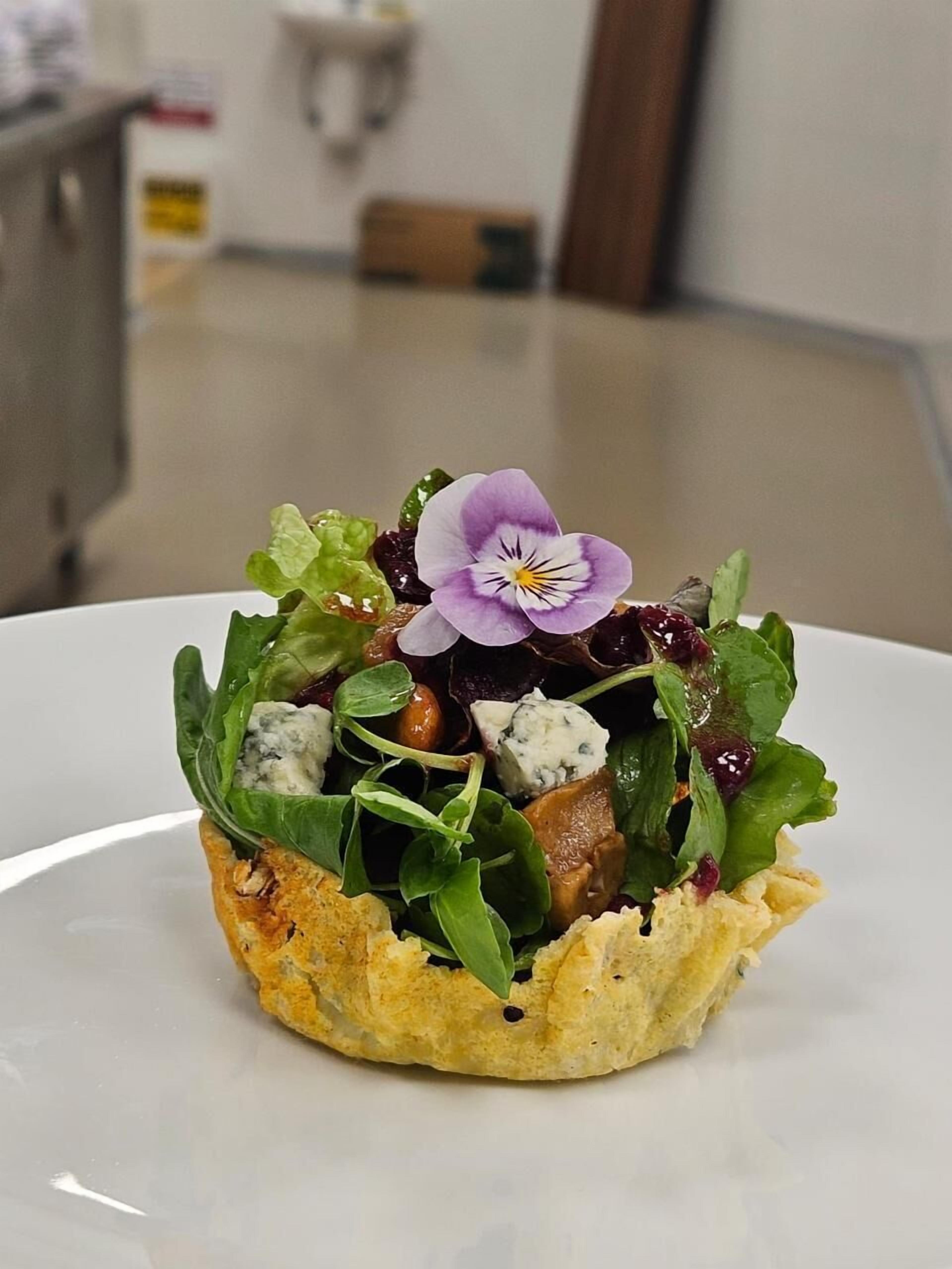 Ein Teller mit Blättern, einer violetten Blüte und einem Stück Brot.