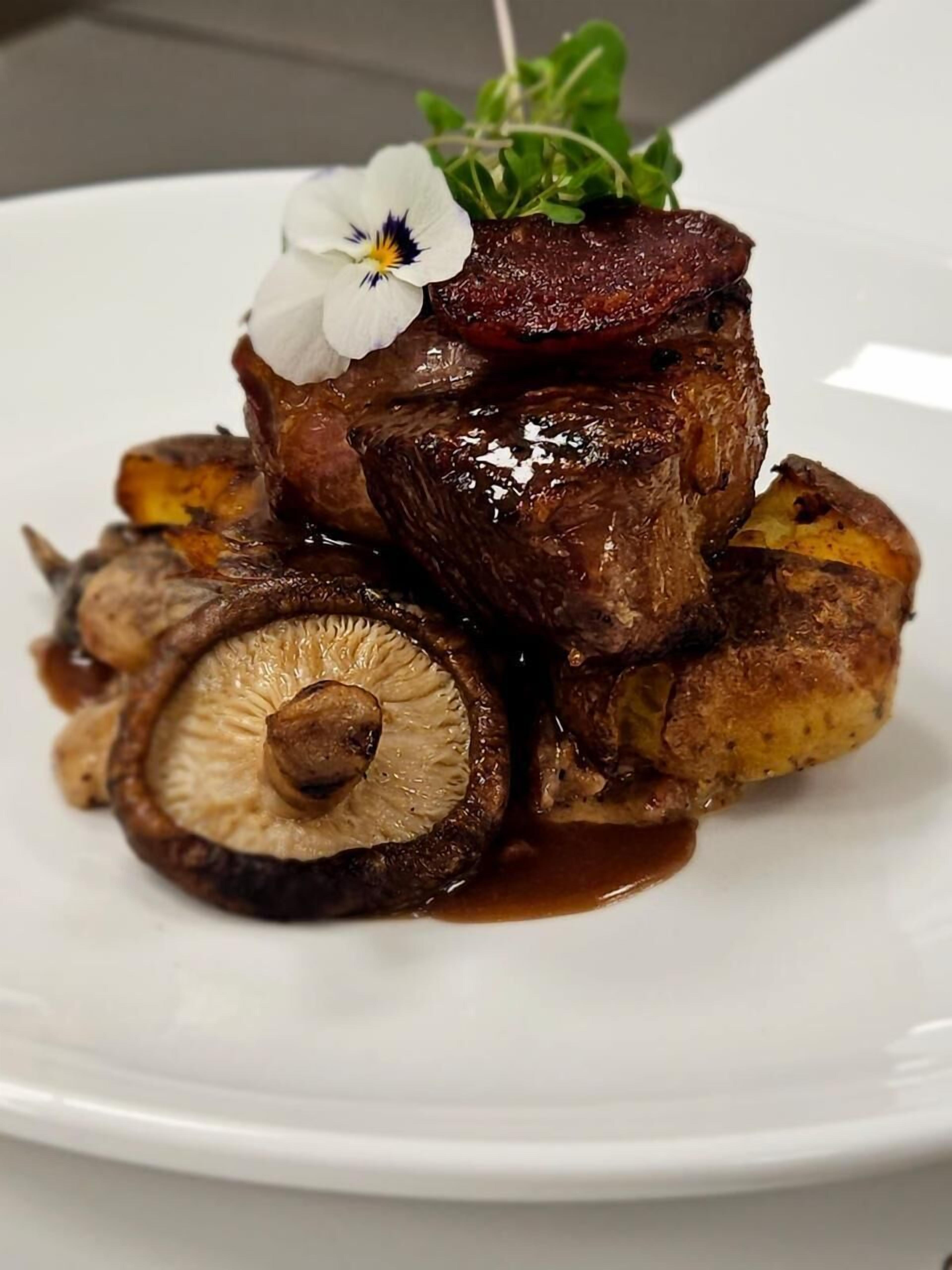 A plate of food with a piece of meat, mushrooms, and a flower garnish.