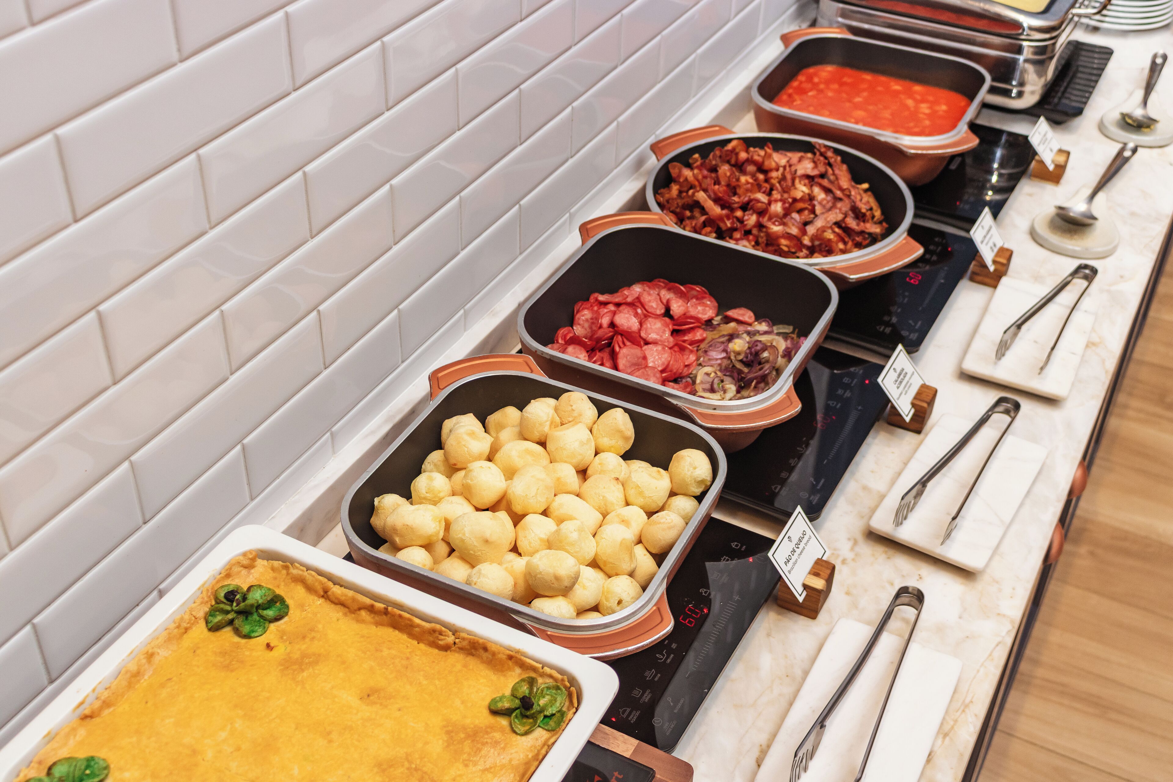 Buffet com diversos alimentos dispostos em bandejas, incluindo torta, batatas e carnes.