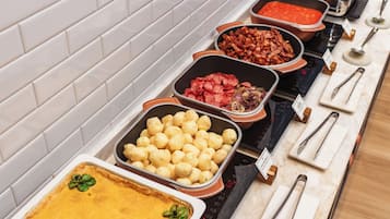 Buffet com diversos alimentos dispostos em bandejas, incluindo torta, batatas e carnes.