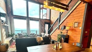 Tilava olohuone, jossa on puinen ruokapöytä, penkit ja portaat, jotka johtavat ylemmälle tasolle.