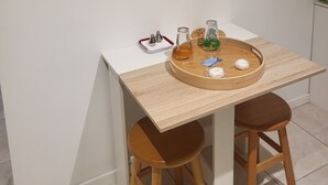Un pequeño comedor con una mesa blanca y dos taburetes de madera. Encima de la mesa, un cuadro de un paisaje invernal.