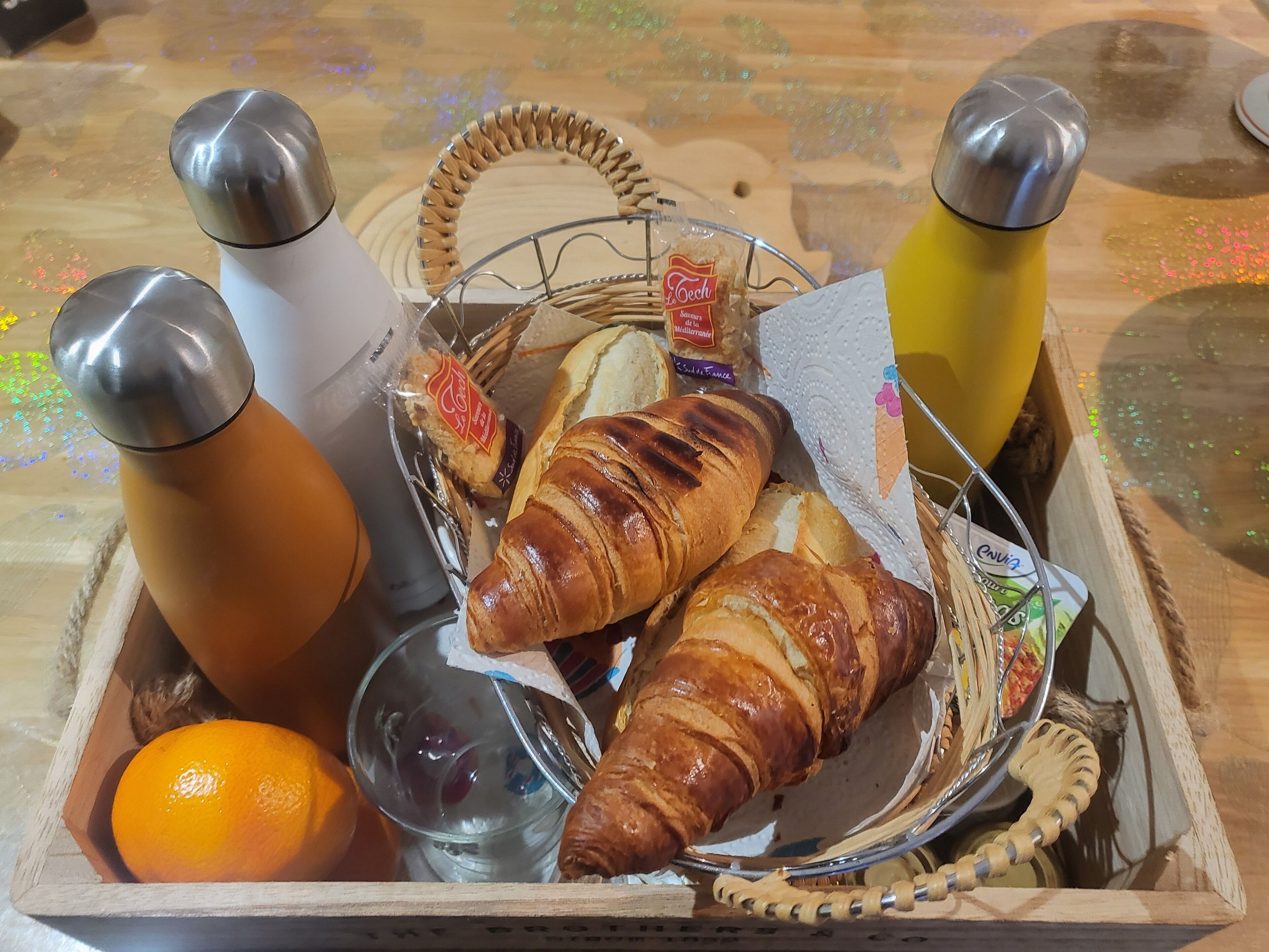 Une boîte en bois contenant un croissant, une orange, un verre d’eau et deux bouteilles.
