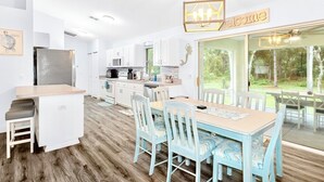 A modern kitchen with white cabinetry, a central island, and a dining area with blue chairs and a wooden table. - Private Crystal River Getaway Minutes to Springs! (Crystal River)