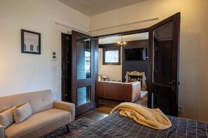 A modern hotel room with a sofa, a bed with a patterned bedspread, a fireplace, and a television. - IVY House | Kansas City (Kansas City)