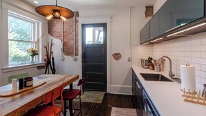 Una cocina moderna con una mesa de madera, sillas rojas, una puerta negra y una ventana con vista a árboles.