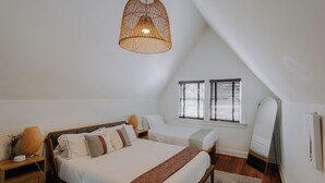 A bedroom with a large bed, bedside tables, a hanging light fixture, a window with blinds, and a mirror.