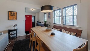 A modern kitchen with a wooden dining table, a red refrigerator, and a large window with blinds.