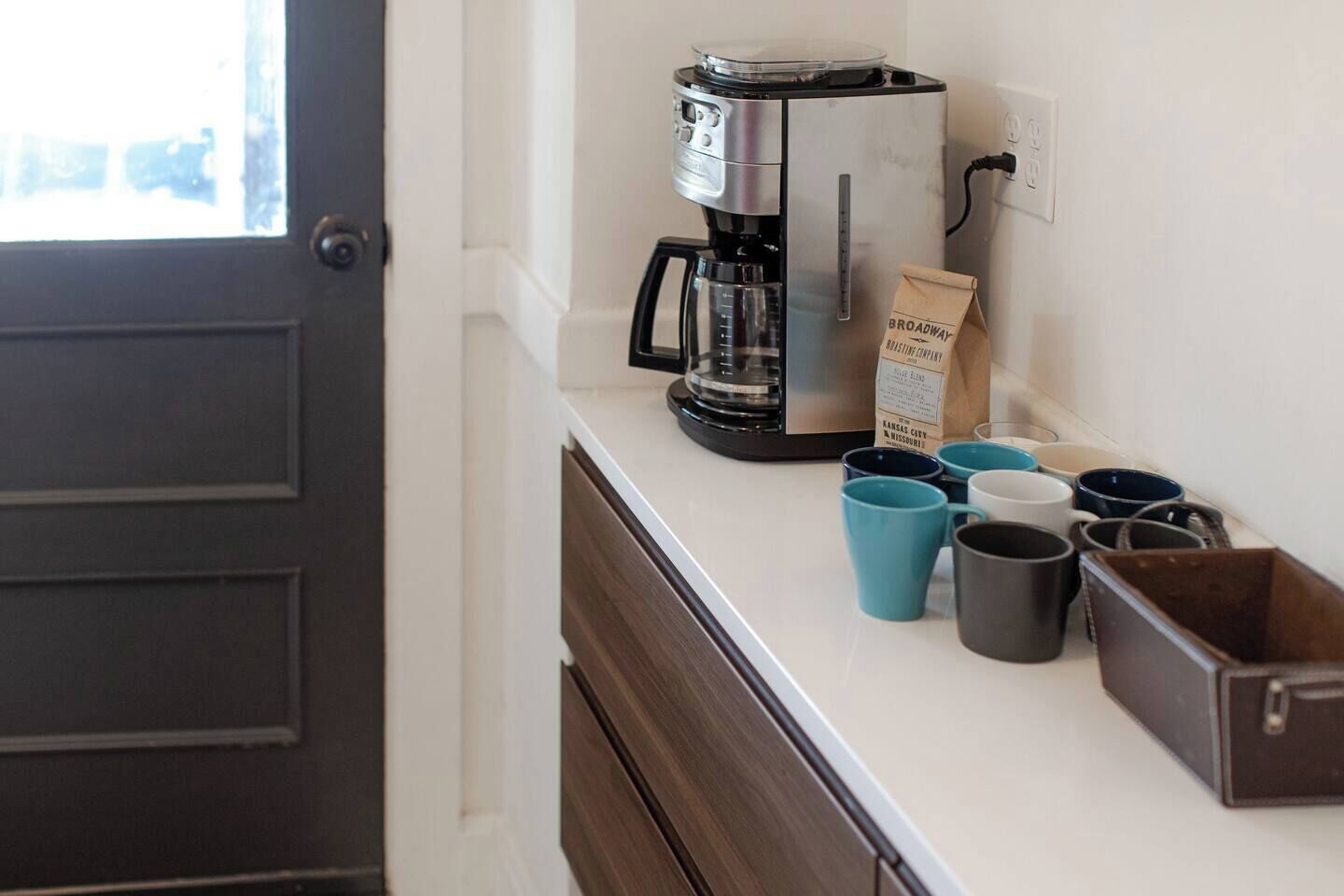 A kitchen counter with a coffee maker, a bag of coffee, and several mugs.