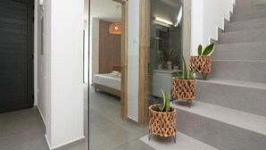 Un intérieur moderne avec un escalier, un lit et deux supports à plantes en osier.