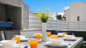 Une table de petit-déjeuner dressée avec des bols, des verres de jus d’orange et un vase rempli de fleurs jaunes.
