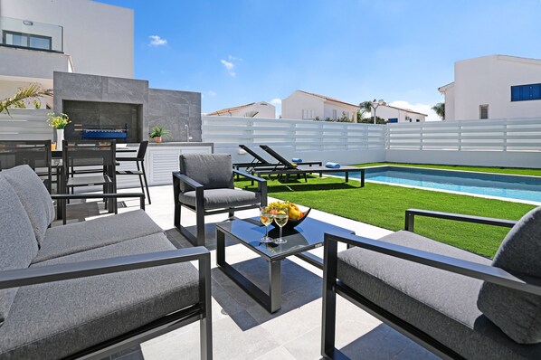 A modern outdoor patio with a pool, grey furniture, and a clear view of the surrounding buildings.
