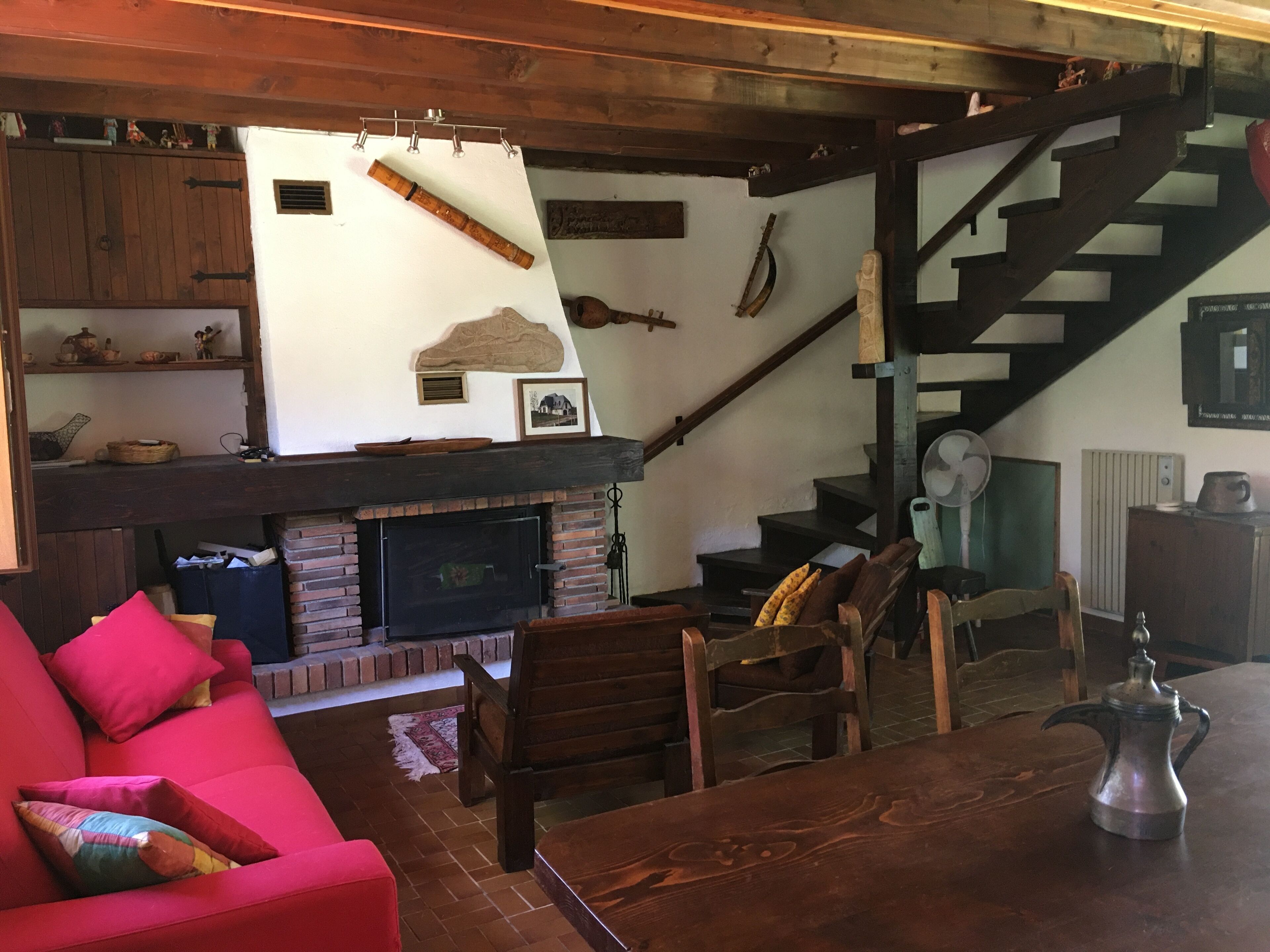 A cozy living room with a fireplace, wooden furniture, and a staircase.