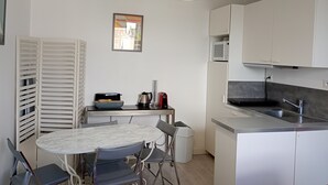 A compact kitchen with white cabinets, a round marble table, and a hanging light fixture.