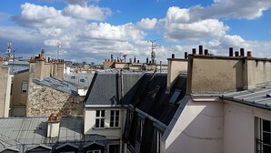A cityscape with multiple rooftops, some with chimneys and satellite dishes, under a partly cloudy sky.