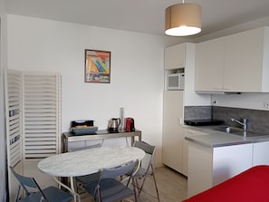 Una cocina compacta con comedor, armarios blancos, un microondas y una lámpara colgante.