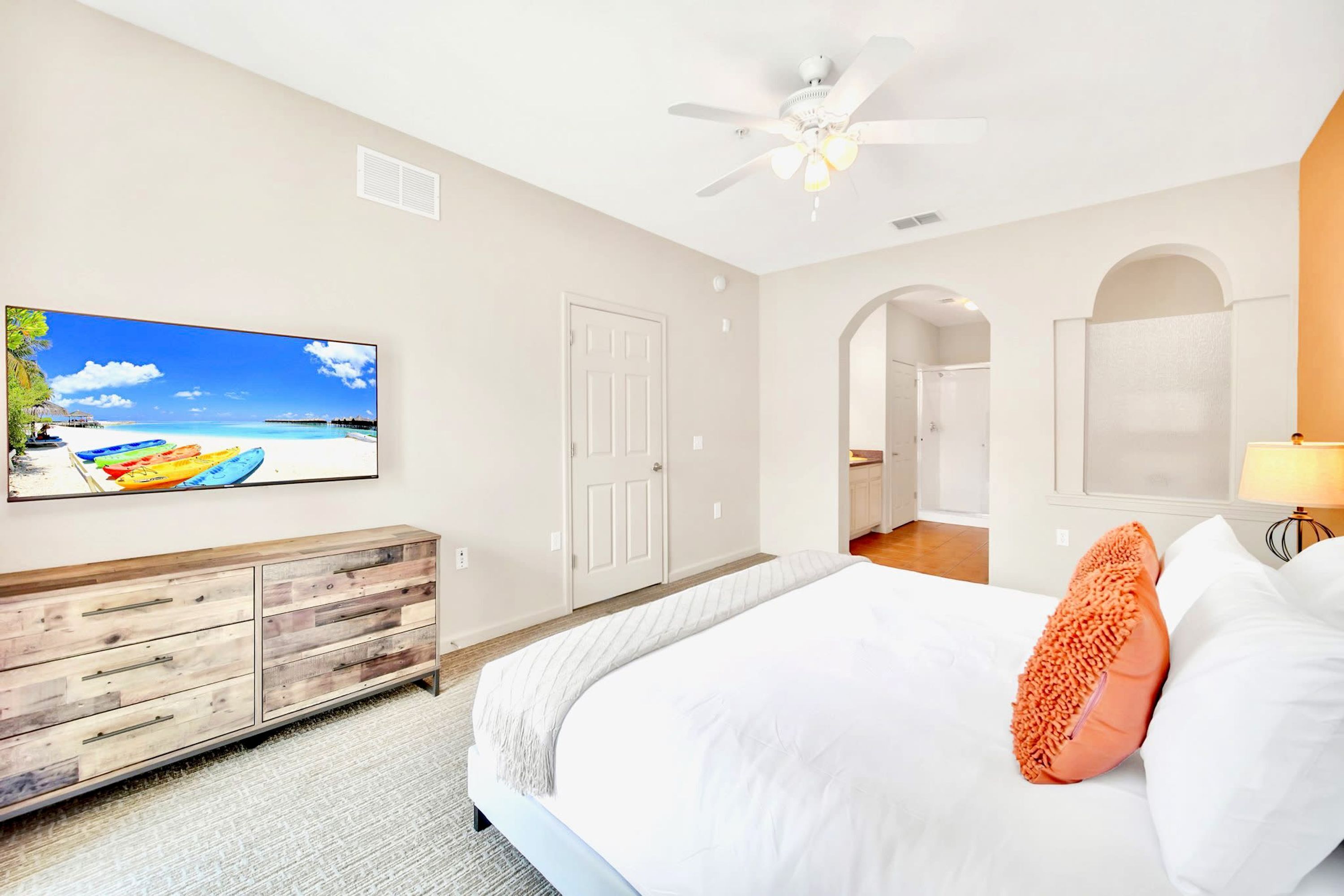 Une chambre à coucher avec un lit, une télévision, un ventilateur de plafond et une vue sur la plage, visible par la fenêtre.