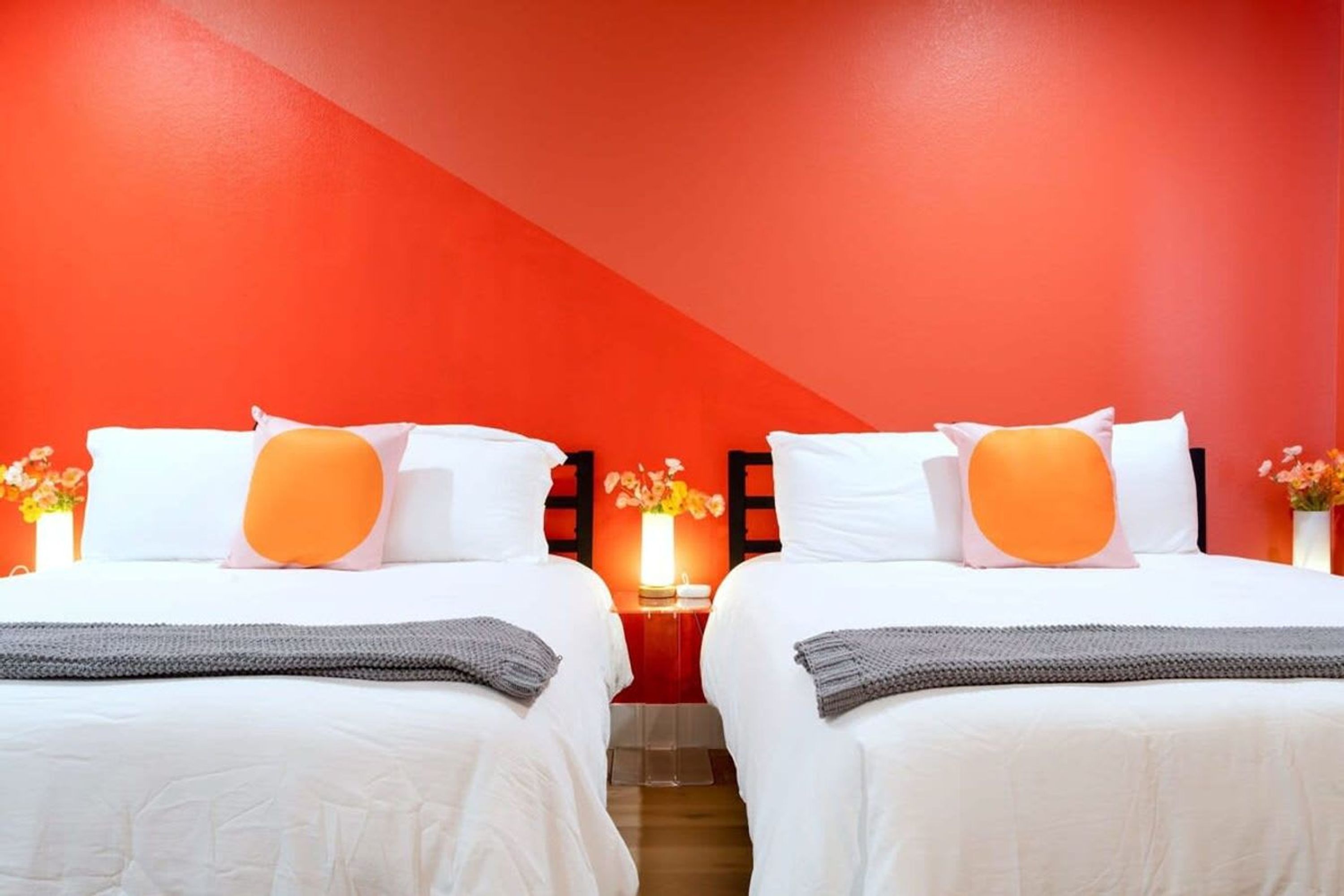 Une chambre d’hôtel avec deux lits, des murs rouges et une petite table sur laquelle est posé un vase de fleurs.