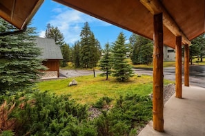 A covered outdoor area with wooden pillars, a stone building, and a road with trees in the background.