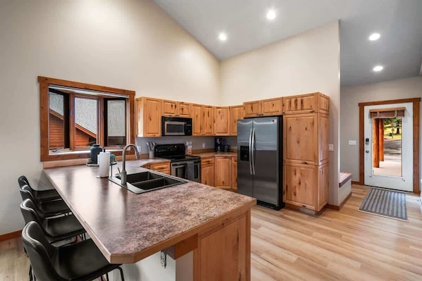 A modern kitchen with wooden cabinets, a granite countertop, stainless steel appliances, and a large window.