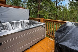 A hot tub on a wooden deck with a view of a forest.