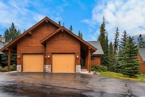 A two-story wooden cabin with a garage, stone accents, and a driveway.