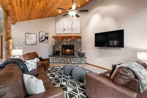 Ein gemütliches Wohnzimmer mit Kamin aus Stein, Ledersofas und einem Flachbildfernseher.