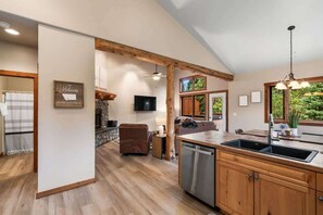 A spacious kitchen with wooden cabinets, a dishwasher, and a large window offering a view of greenery. - 3-Bed Big Sky Townhome w/ Private Hot Tub (Big Sky)