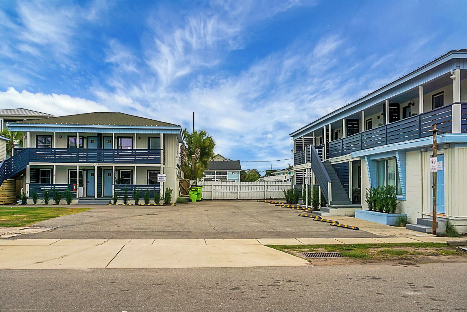 A two-story motel with a blue and white exterior, a covered parking area, and a small front yard with plants.