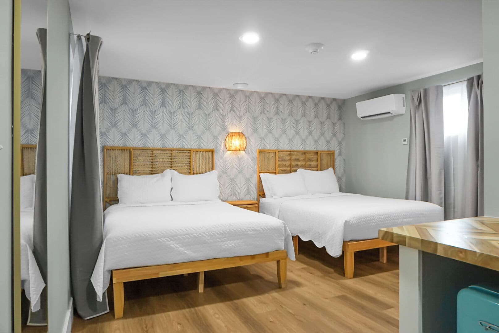 Habitación de hotel con dos camas, cabecero de madera, lámpara de pared y unidad de aire acondicionado, además de un escritorio de madera.