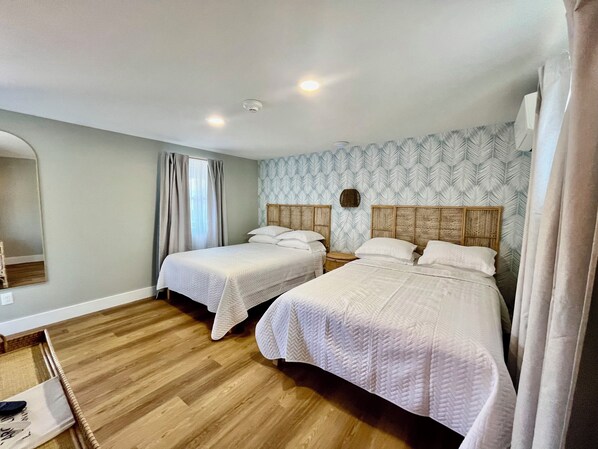 A hotel room with two beds, wooden flooring, a large mirror, and a patterned wall. - Carolina Beach Motel (Carolina Beach)