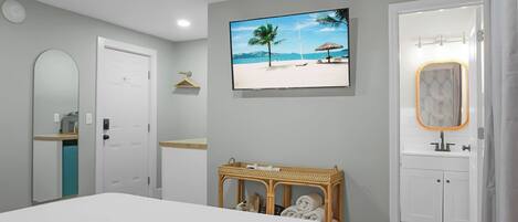 A bedroom with a bed, a television displaying a beach scene, a mirror, and a door leading to a bathroom.