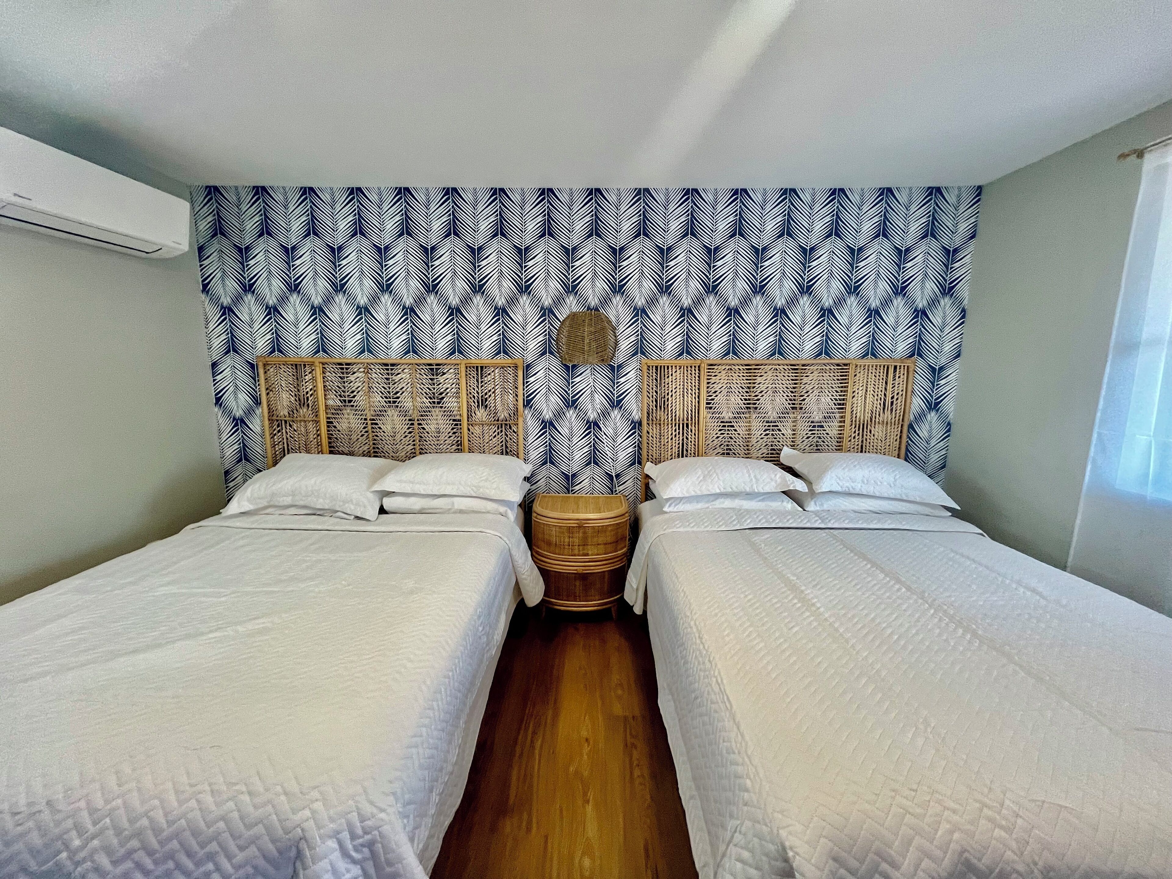 Une chambre avec deux lits, une tête de lit en osier et un mur décoré d’un motif.