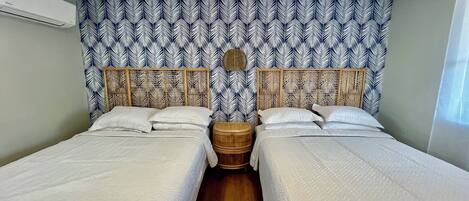 A room with two beds, a woven headboard, and a patterned wall.