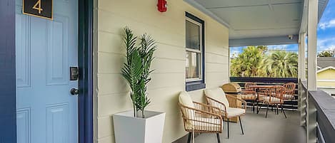 A covered porch with a blue door marked "No 4", wicker chairs, a potted plant, and a view of palm trees.