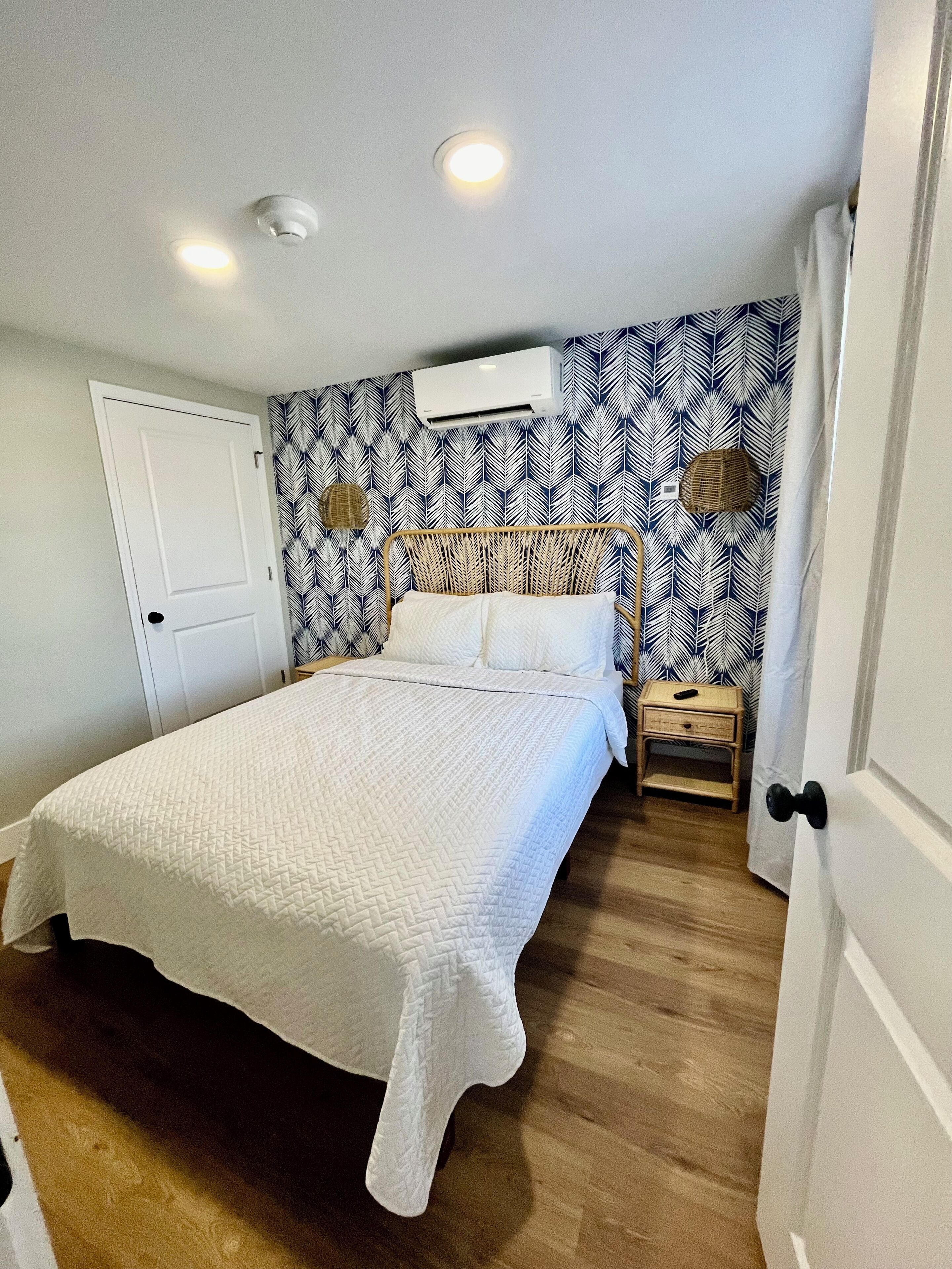 A bedroom with a bed, a nightstand, a wall-mounted air conditioner, and a door.