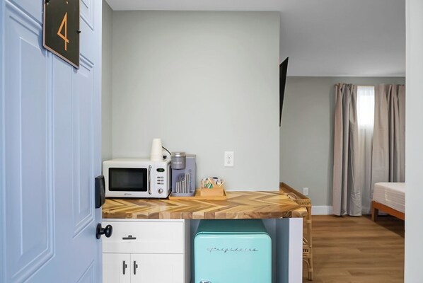 Una kitchenette compacta con microondas, cafetera y un refrigerador pequeño.