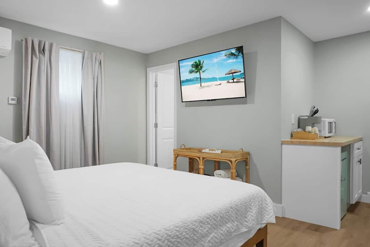 Hotellihuone, jossa on sänky, pieni pöytä, seinälle asennettu televisio ja pieni keittiönurkkaus.
