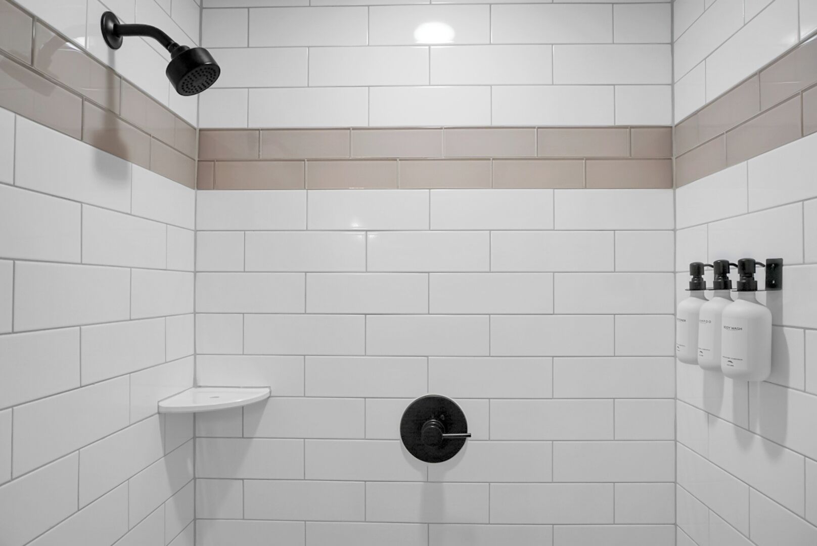 A modern shower with a handheld showerhead, a wall-mounted toilet, and a shelf with toiletries.