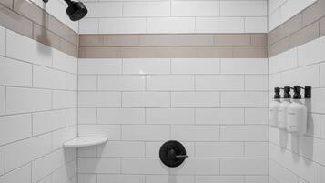 A modern shower with a handheld showerhead, a wall-mounted toilet, and a shelf with toiletries.