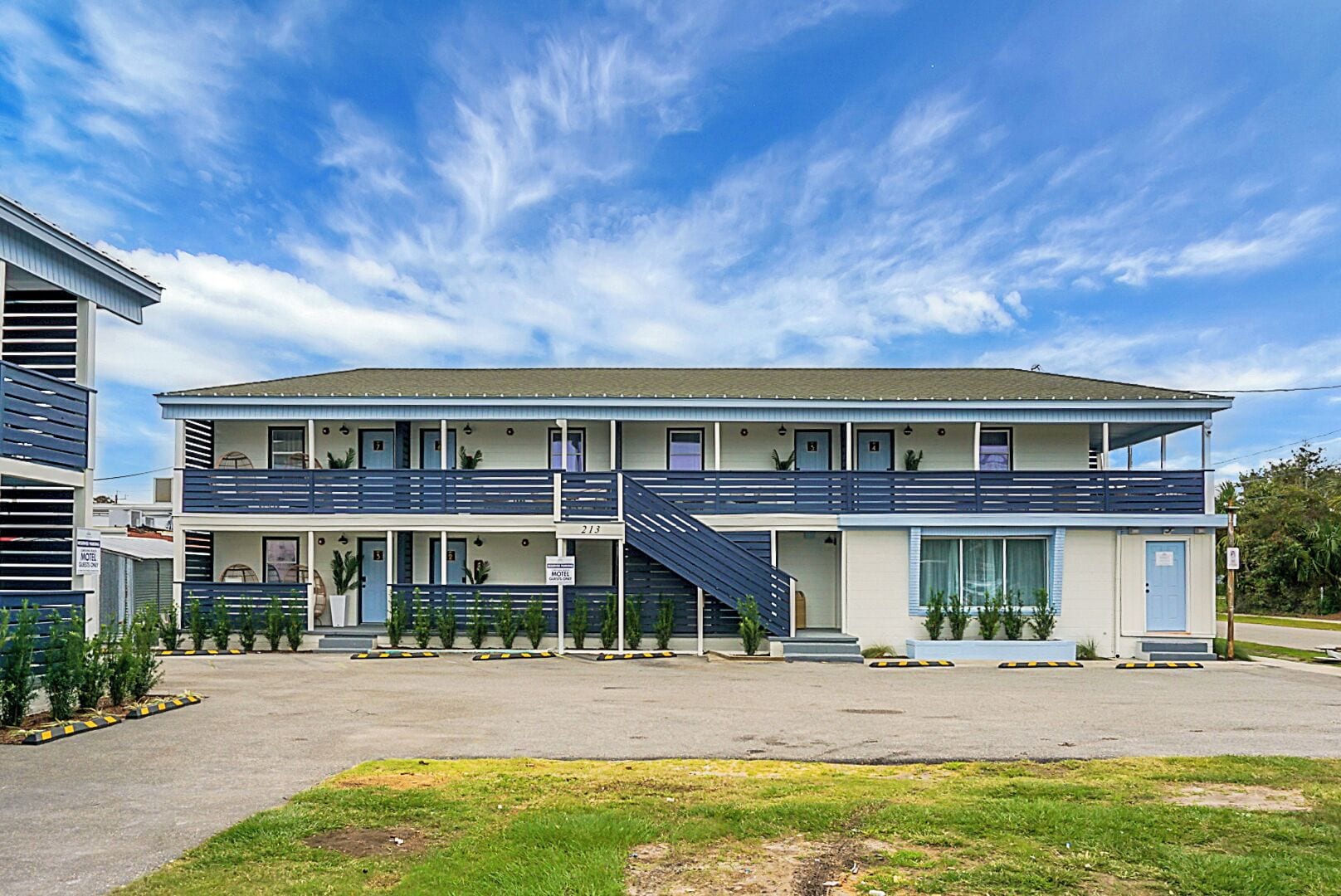 A motel with two-story buildings, a covered parking area, and a grassy front lawn.