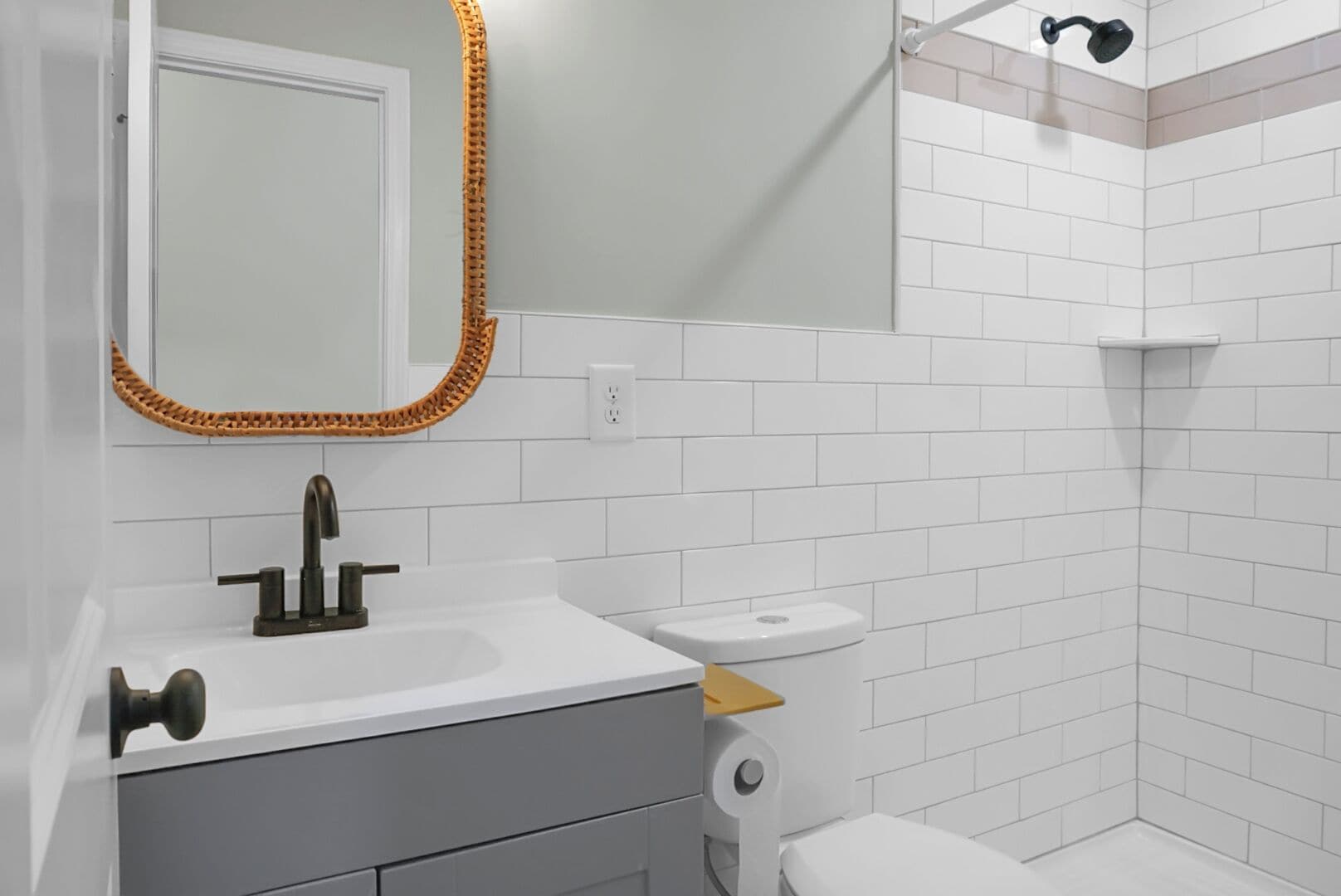 A bathroom with a white sink, a mirror with a woven frame, a toilet, and a shower area.