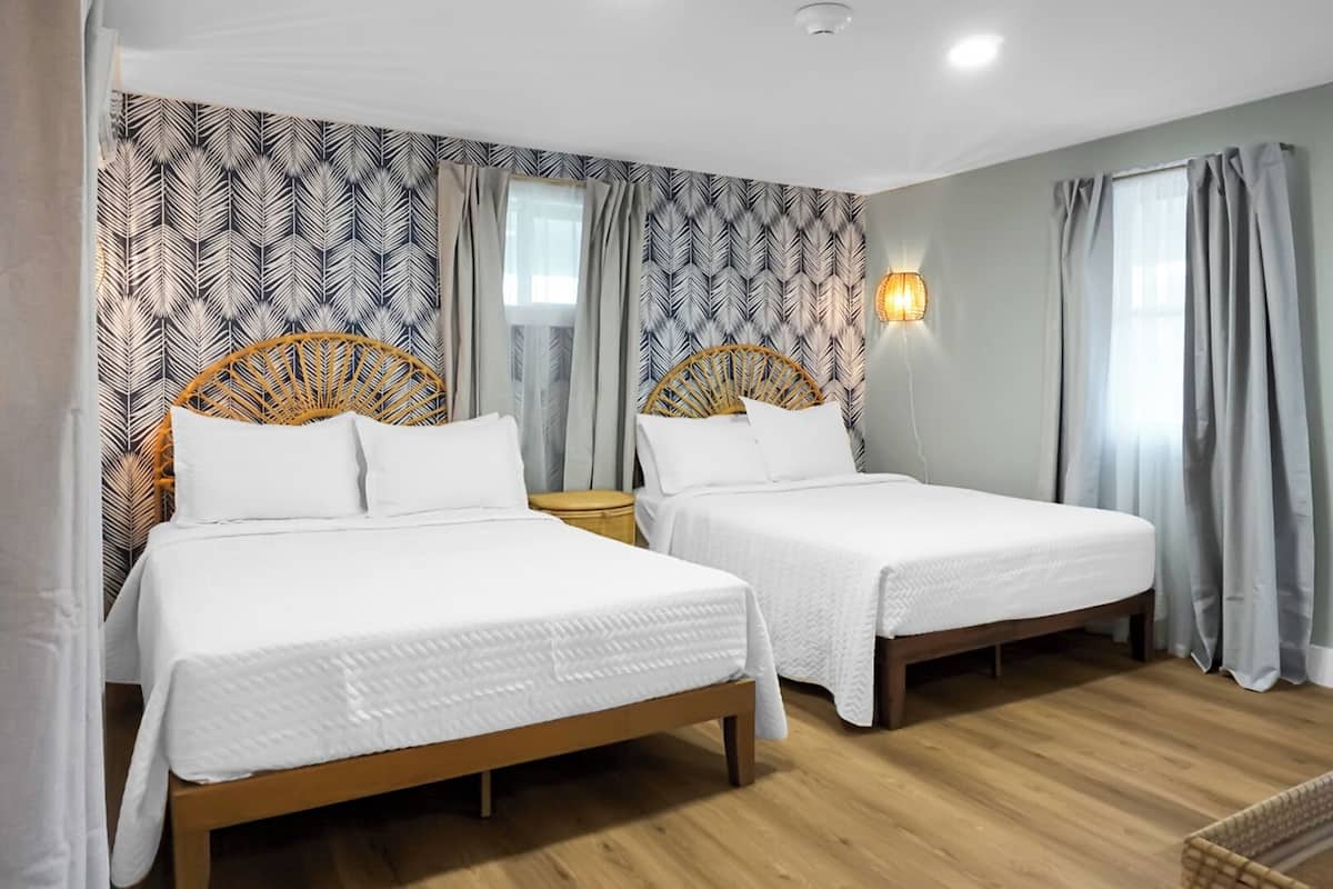 Hotellihuone, jossa on kaksi erillistä sänkyä, puulattia ja kuviollinen tapetti.