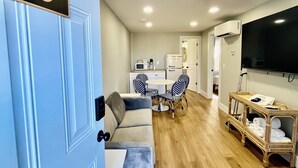A modern living room with a blue door marked "No 8", a grey sofa, a dining table with chairs, and a TV mounted on the wall.