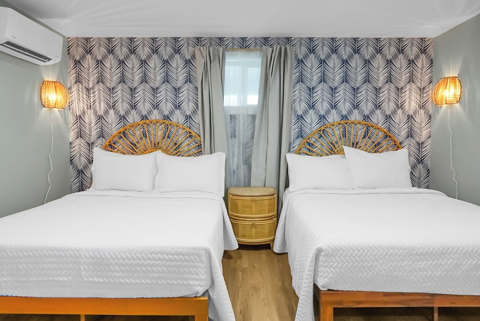 A double room with two beds, each with a wicker headboard, white bedding, and a small wooden nightstand.