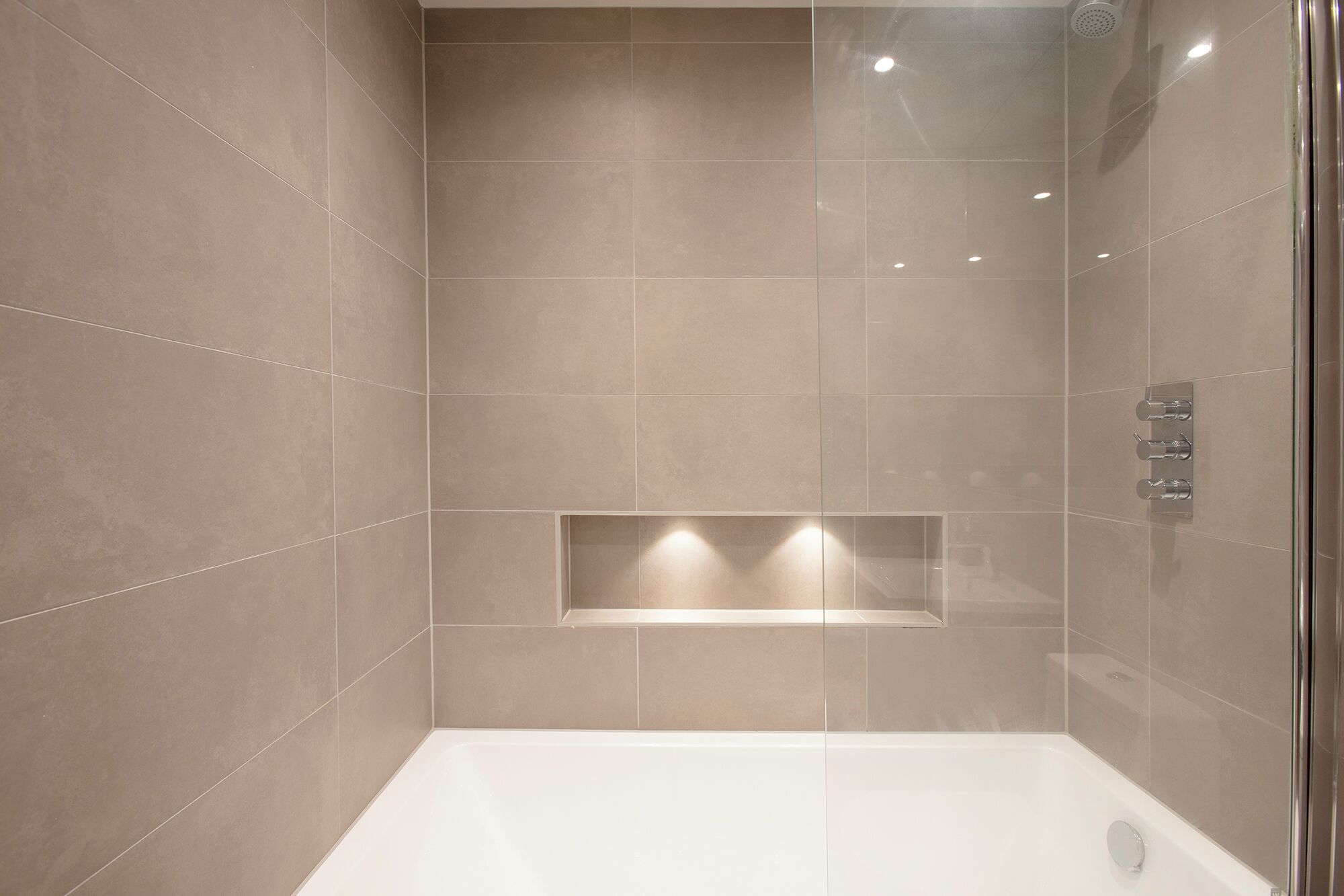 Een moderne badkamer met een douchecabine van glas, een inbouwbank en een wit bad.