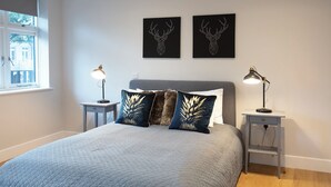 A bedroom with a bed, two bedside tables, two lamps, a window, and two wall art pieces. - Hampden Apartments - The Edward (Windsor)