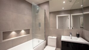 A modern bathroom with a glass-enclosed shower, a white toilet, and a vanity with a sink and mirror. - Hampden Apartments - The Edward (Windsor)