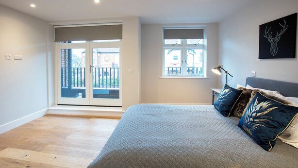 A bedroom with a bed, a desk, a chair, a window, and a balcony. - Hampden Apartments - The Edward (Windsor)