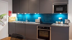 A modern kitchen with dark cabinets, a stainless steel sink, a toaster, a kettle, and a built-in oven. - Hampden Apartments - The Edward (Windsor)